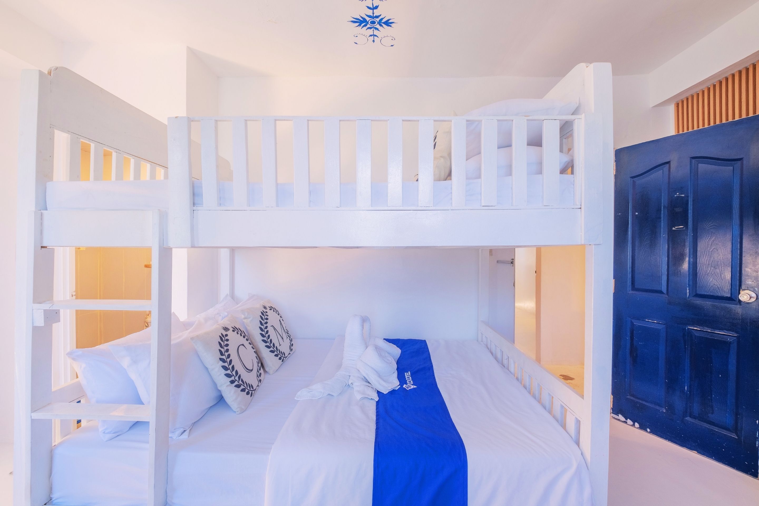 A bunk bed room with a blue towel and pillows, a white door, and a ceiling decoration.
