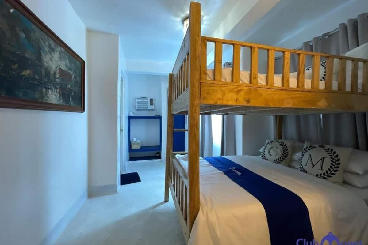 Un lit superposé avec une couverture bleue, un tableau accroché au mur et un petit bureau avec une chaise.