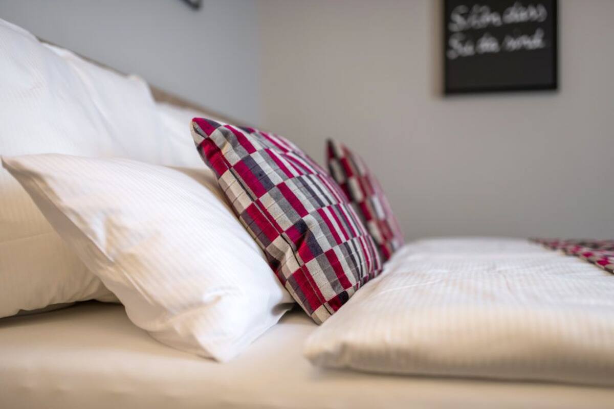 A bed with white and plaid pillows, a white comforter, and a black sign on the wall.