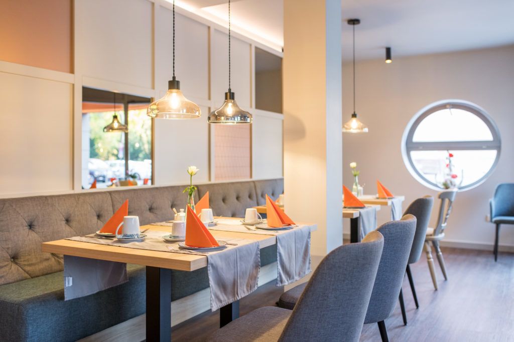 A modern dining area with multiple tables, grey upholstered seating, and pendant lighting.