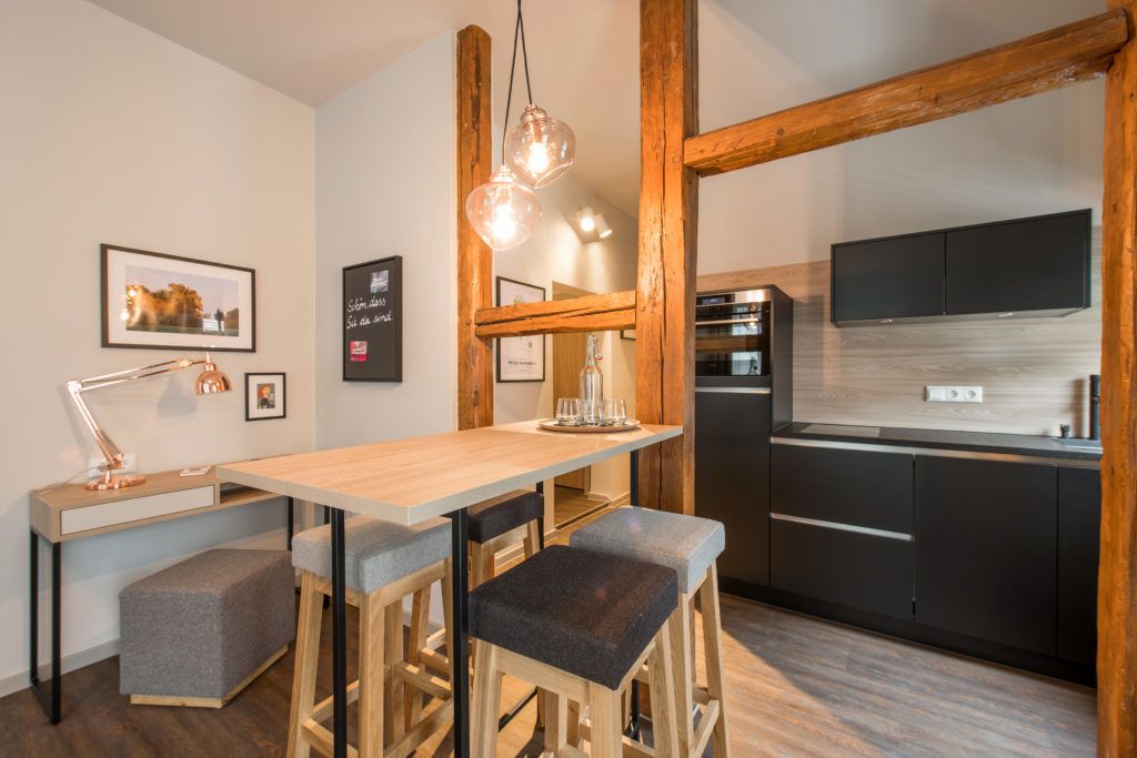 A modern kitchen with wooden stools, a wooden table, and pendant lighting.