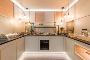 A modern kitchen with a central island, overhead lighting, and various food items displayed on the counter. - stattHotel (Weimar)