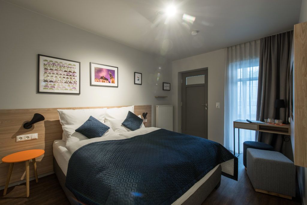 Una habitación de hotel con cama, escritorio, silla y ventana con cortinas.