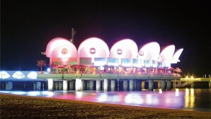 Ein Gebäude am Wasser mit mehreren Bogenstrukturen, einem überdachten Außenbereich und einer Brücke dorthin.