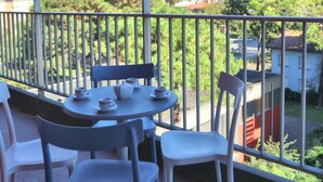 Ein Balkon mit einem für Tee gedeckten Tisch, umgeben von Stühlen, mit Blick auf einen Garten und Gebäude.