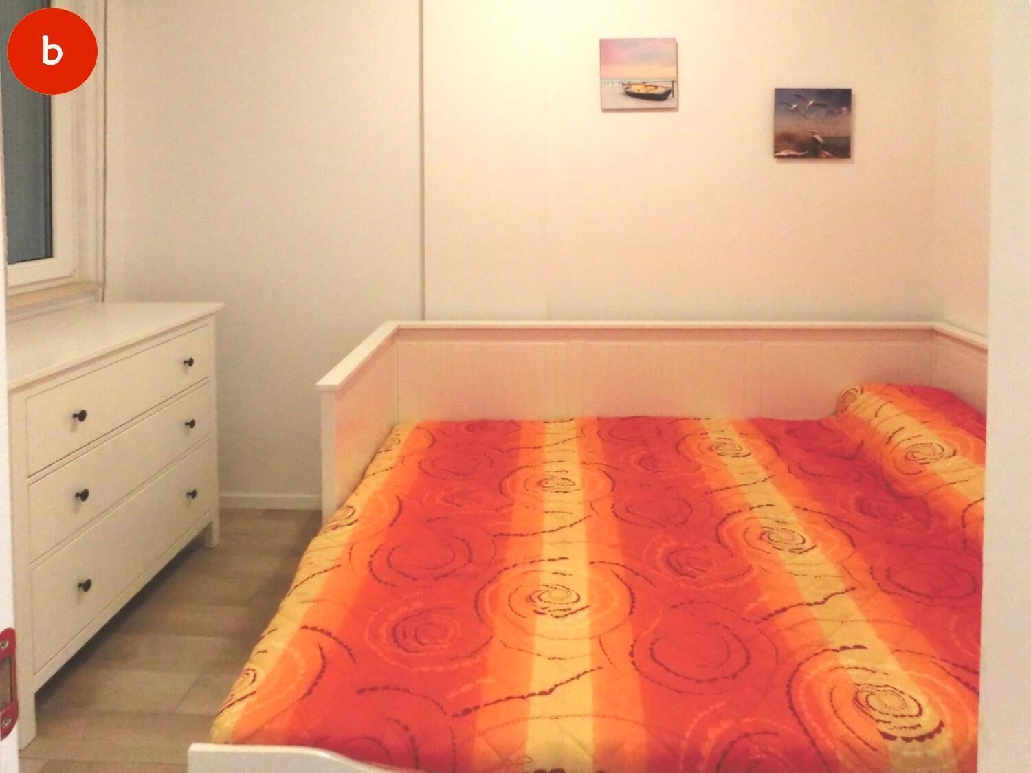 Un dormitorio con una cama, un aparador y dos cuadros en la pared.