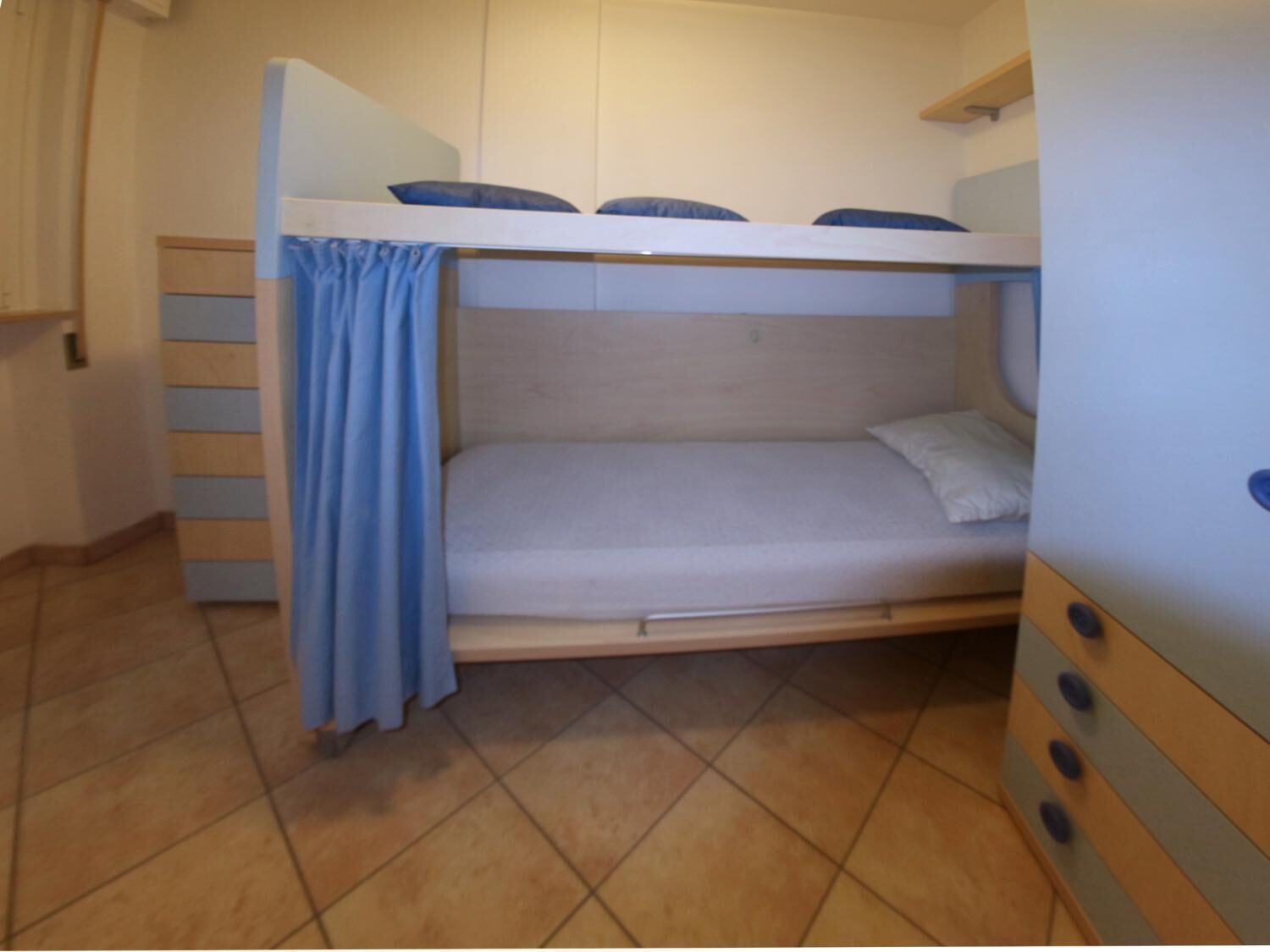 A bunk bed with a curtain, a wooden dresser, and a tiled floor.