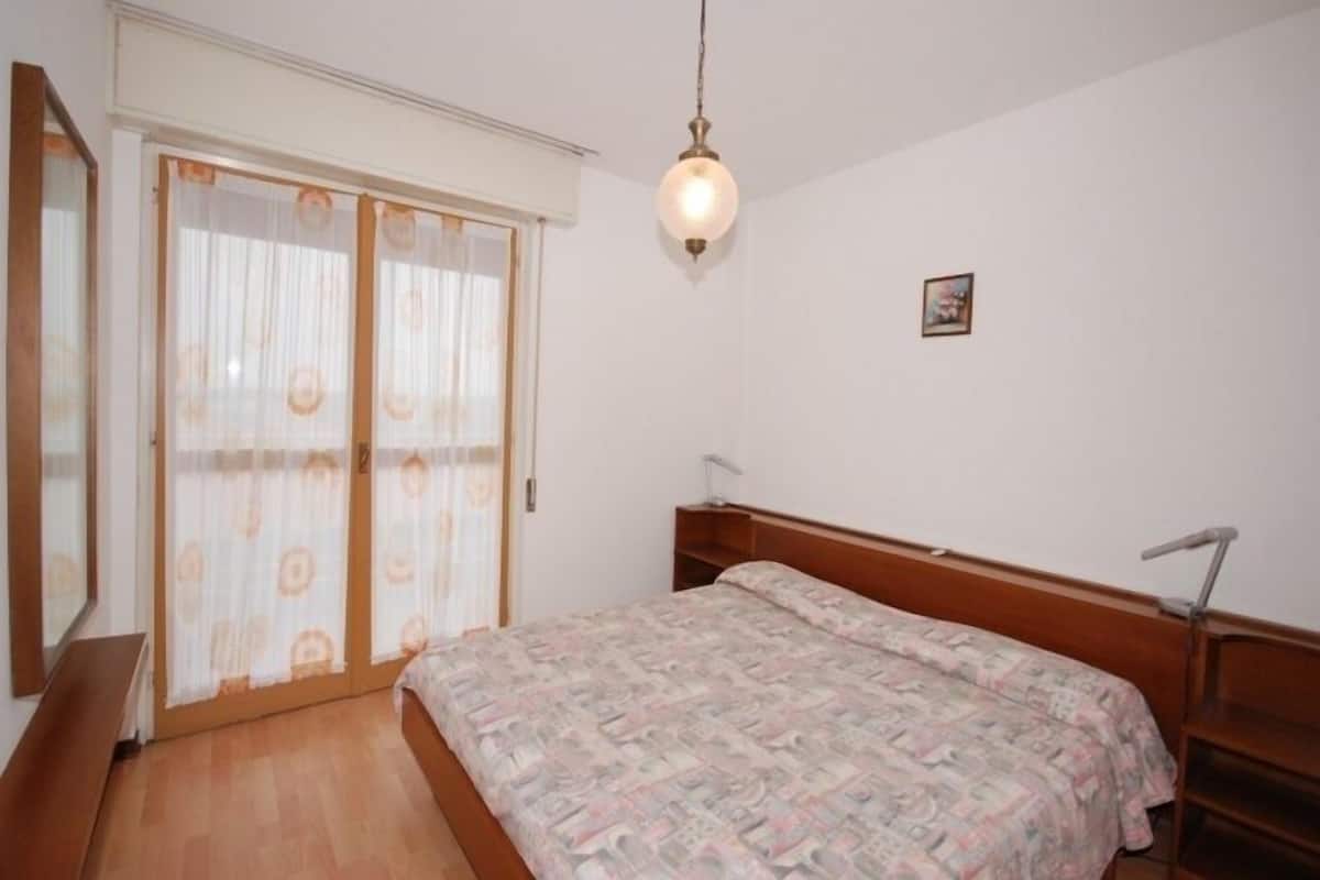 A bedroom with a bed, a wooden headboard, a hanging light fixture, and a sliding door with curtains.