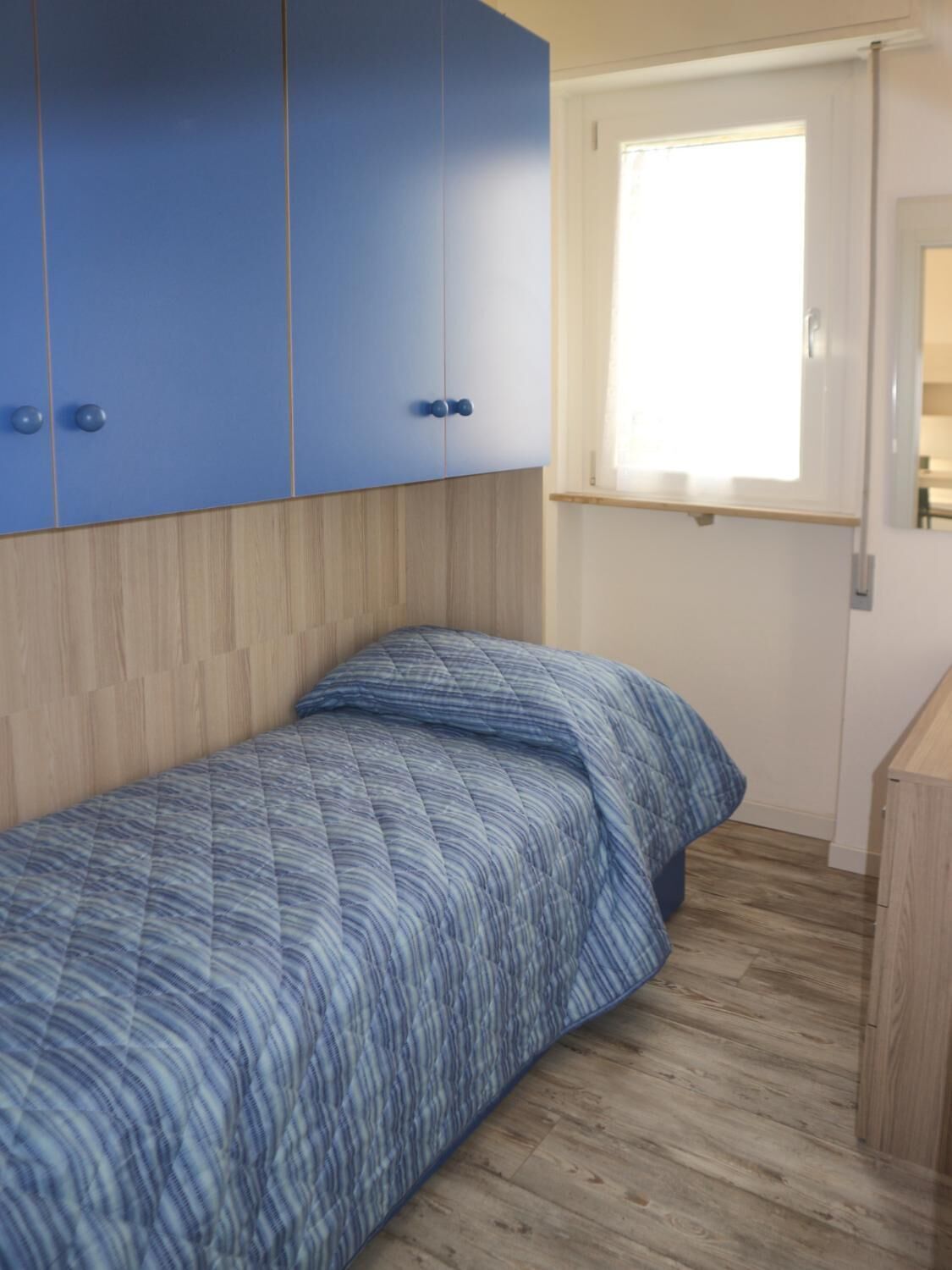 Een slaapkamer met een bed, houten vloeren en blauwe kasten.
