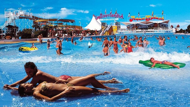Ein großer Außenpool mit mehreren Bahnen, einer Wasserrutsche und im Hintergrund ein Schiff namens 'Culturallandia Aquarium'.