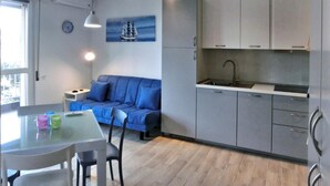 Eine moderne Küche mit grauen Schränken und einer eingebauten Spüle. Im Wohnbereich befindet sich ein Esstisch mit Stühlen sowie ein blaues Sofa.
