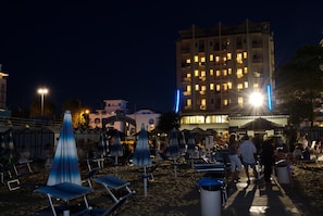 A beachside hotel with multiple floors, outdoor seating areas, and a well-lit facade. - Hotel Kent (Riccione)