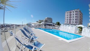 A rooftop pool area with sun loungers and a swimming pool, surrounded by buildings.