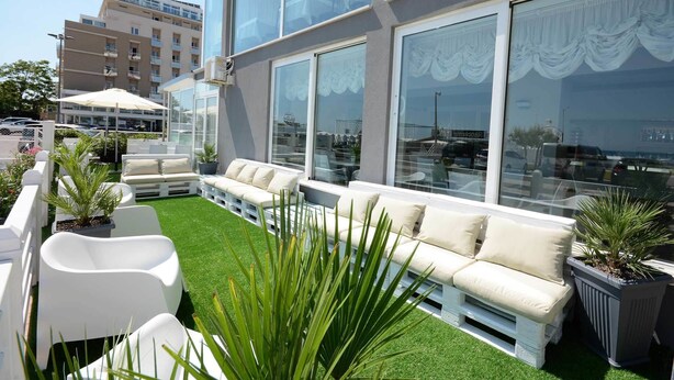 A modern outdoor seating area with white sofas and chairs, surrounded by artificial grass and potted plants.