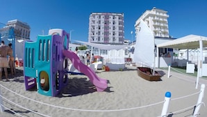 A beach area with a children's play structure, a sailboat model, and a building in the background.