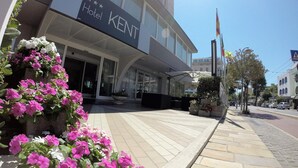 A hotel entrance with a sign reading "Hotel Kent," outdoor seating, and a clear sky.