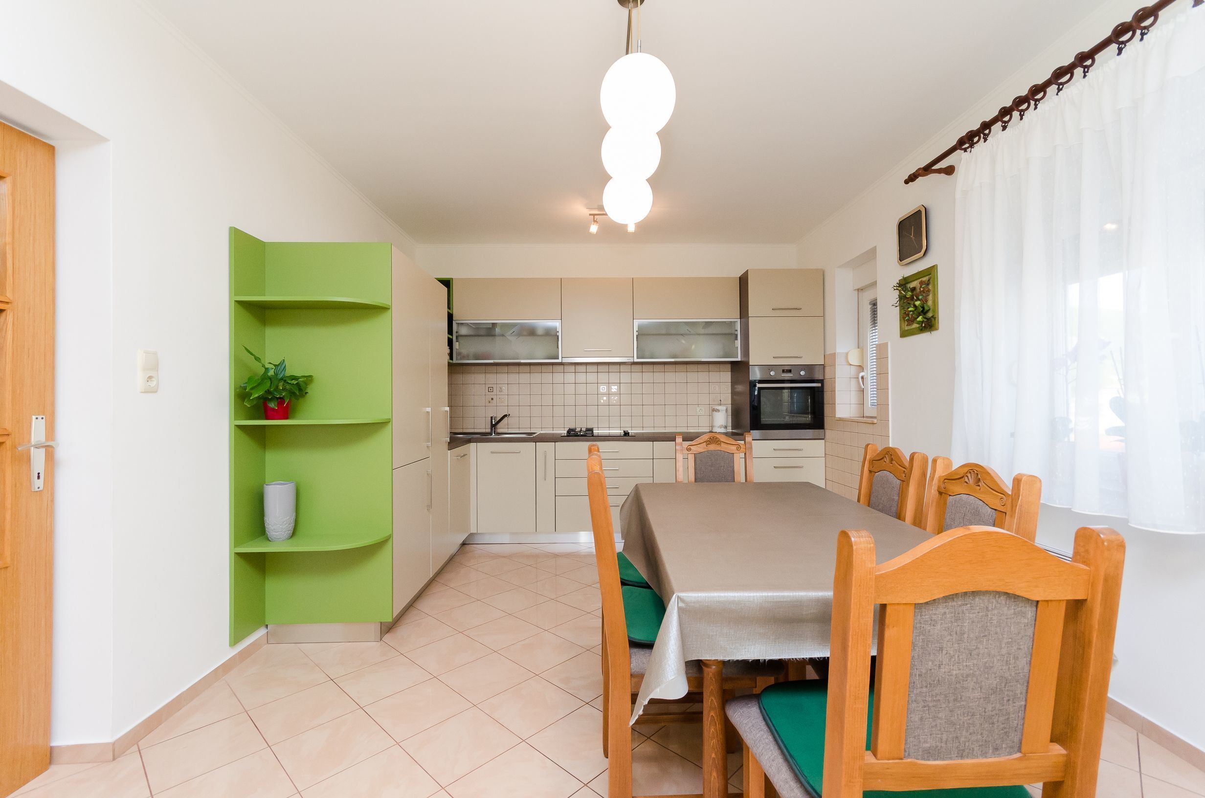 Una cocina moderna con armarios blancos, un estante verde y una mesa de comedor con sillas de madera.