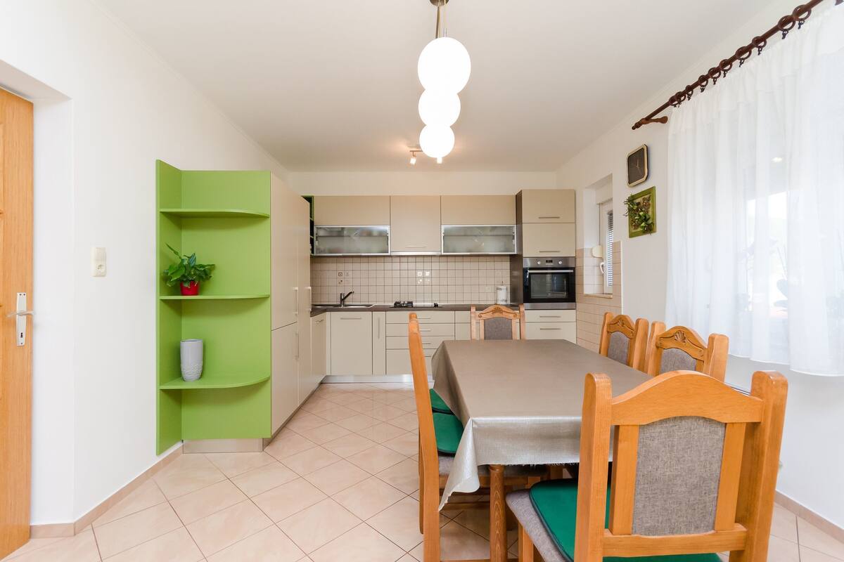 A modern kitchen with white cabinets, a green shelf unit, and a dining table with wooden chairs.