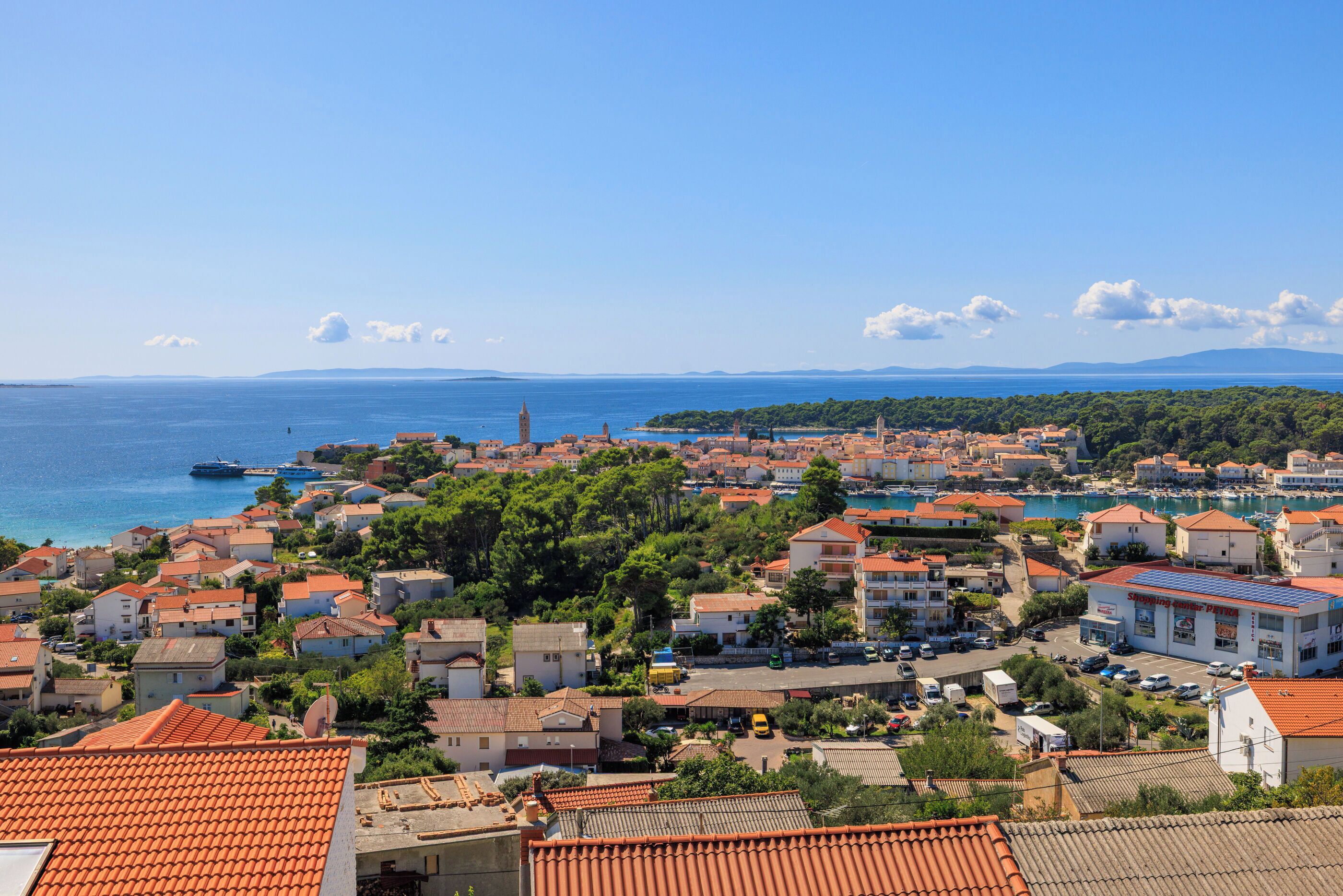 A coastal town with red-tiled roofs, a prominent tower, and a clear view of the sea.