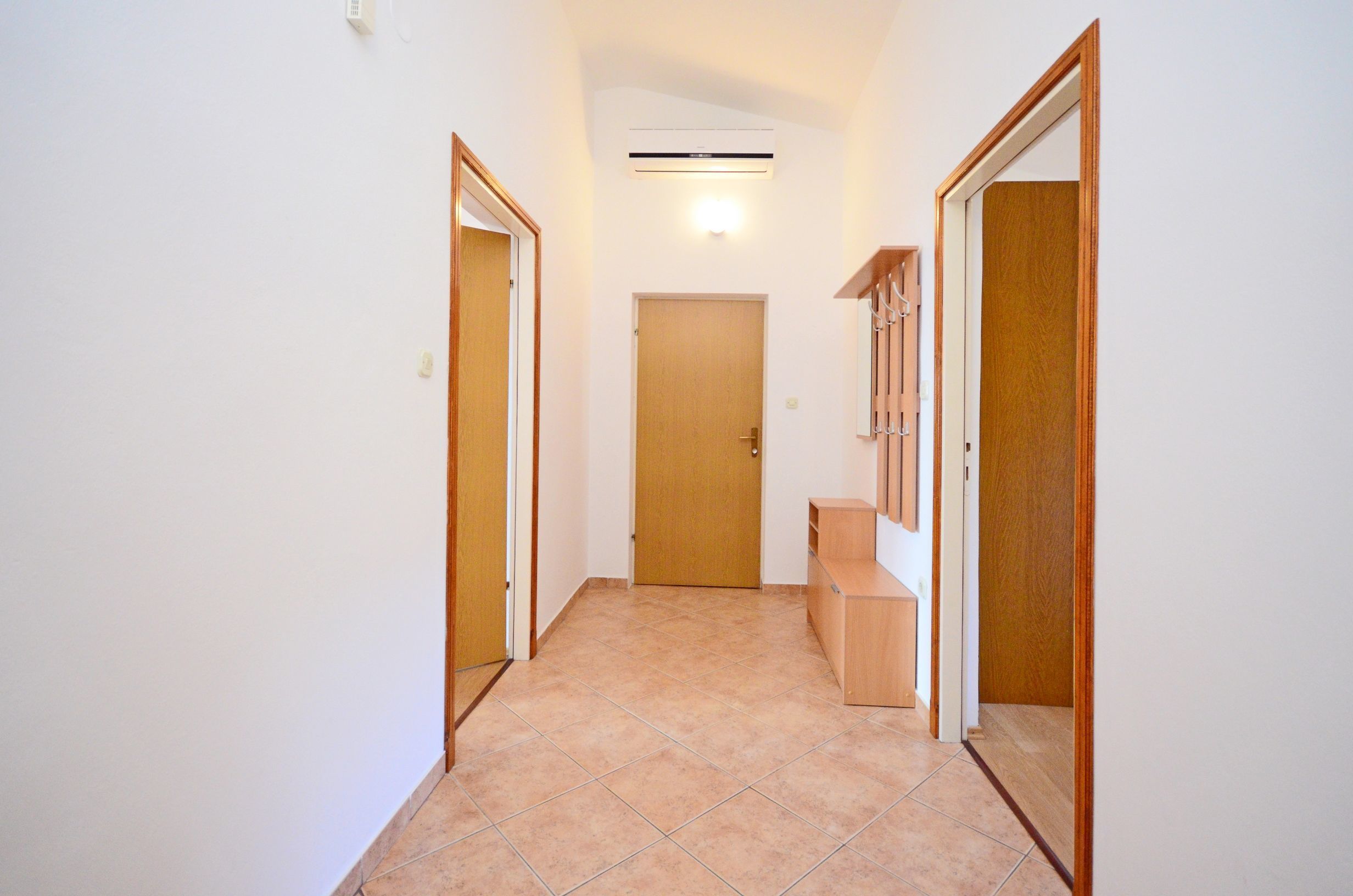 Un pasillo estrecho con suelo de baldosas, puertas de madera y una estantería empotrada.