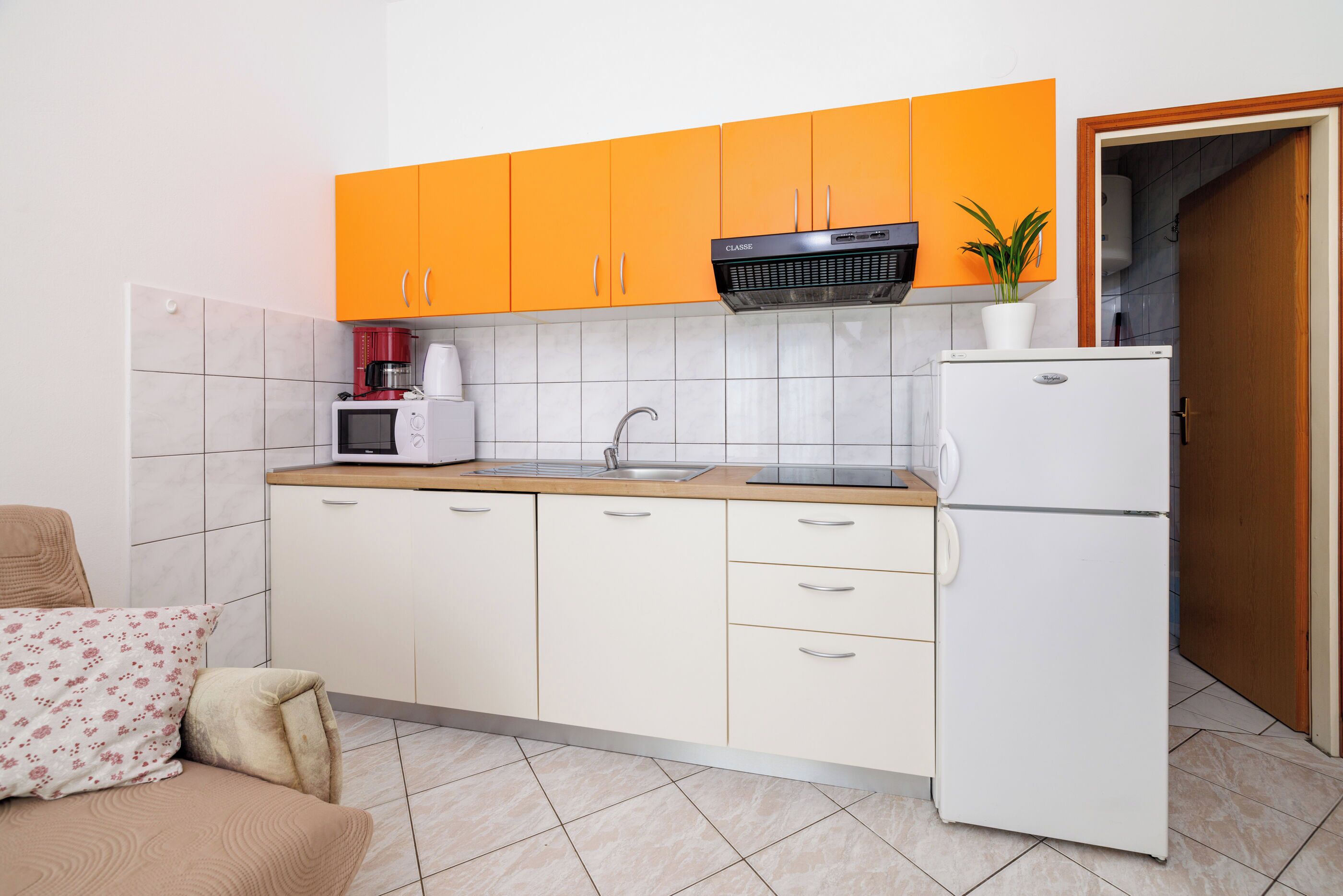 Eine kleine Küche mit orangenen Oberschränken, einem weißen Kühlschrank, einer Mikrowelle und einem Spülbecken.