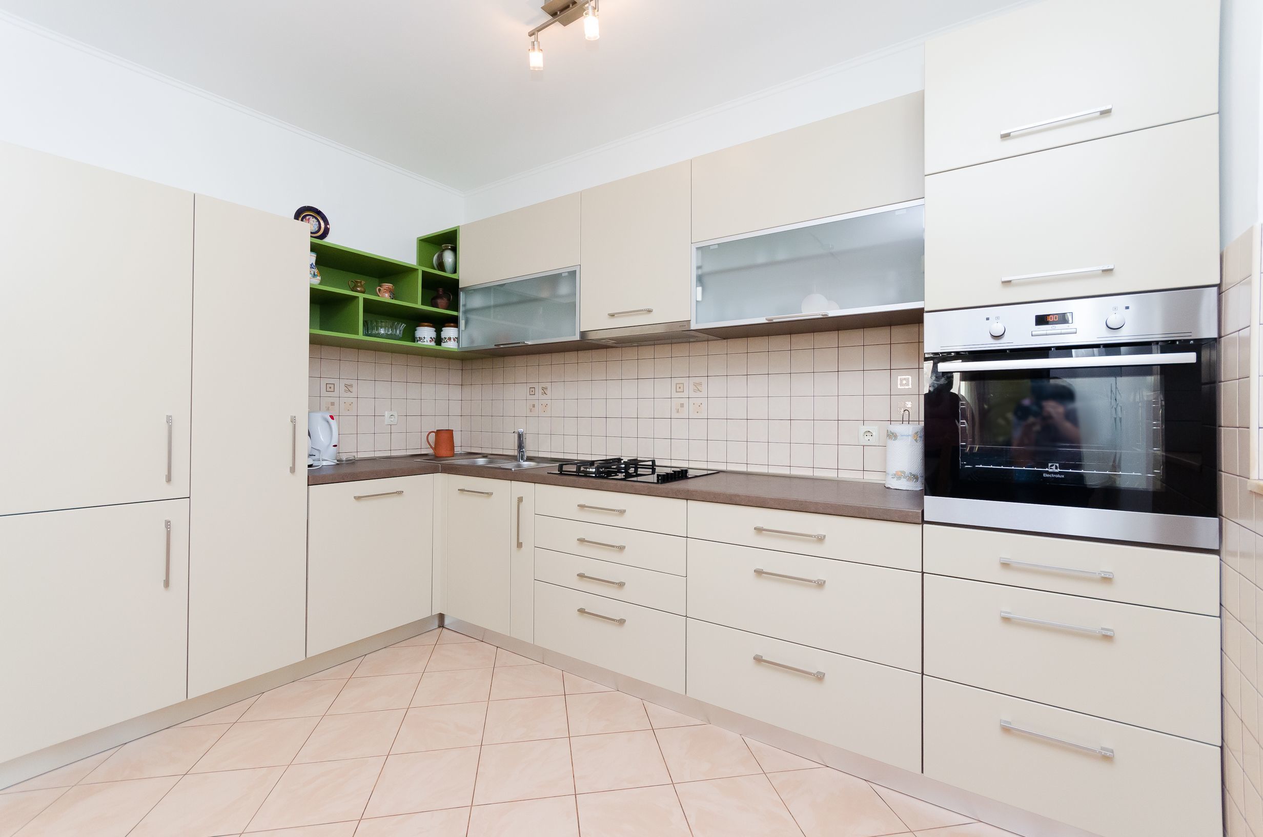 Eine moderne Küche mit weißen Schränken, einem Edelstahlbackofen und einem grünen Regal.