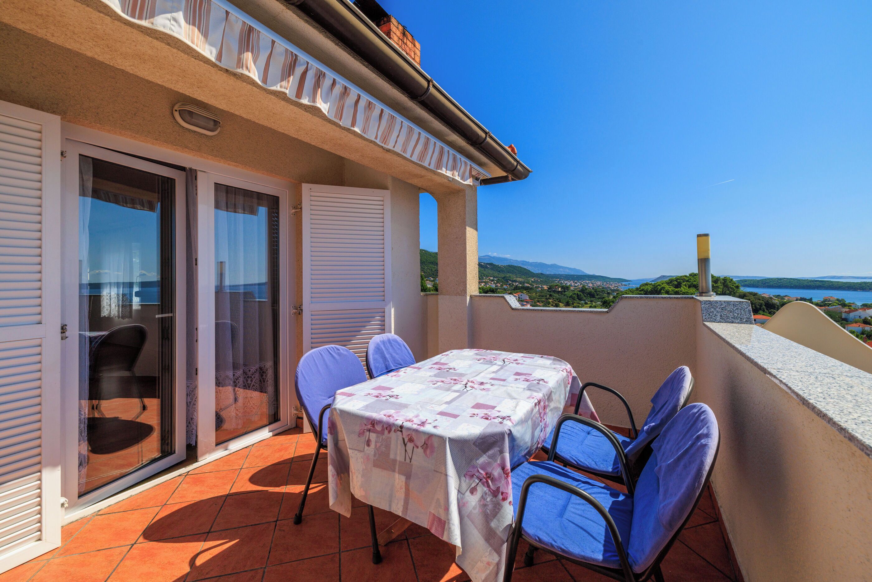 A balcony with a table and chairs, a sliding glass door, and a view of the landscape.