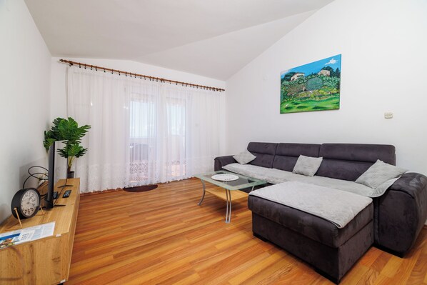 Uma sala de estar moderna com um sofá cinza escuro, uma mesa de centro de vidro e um piso de madeira.