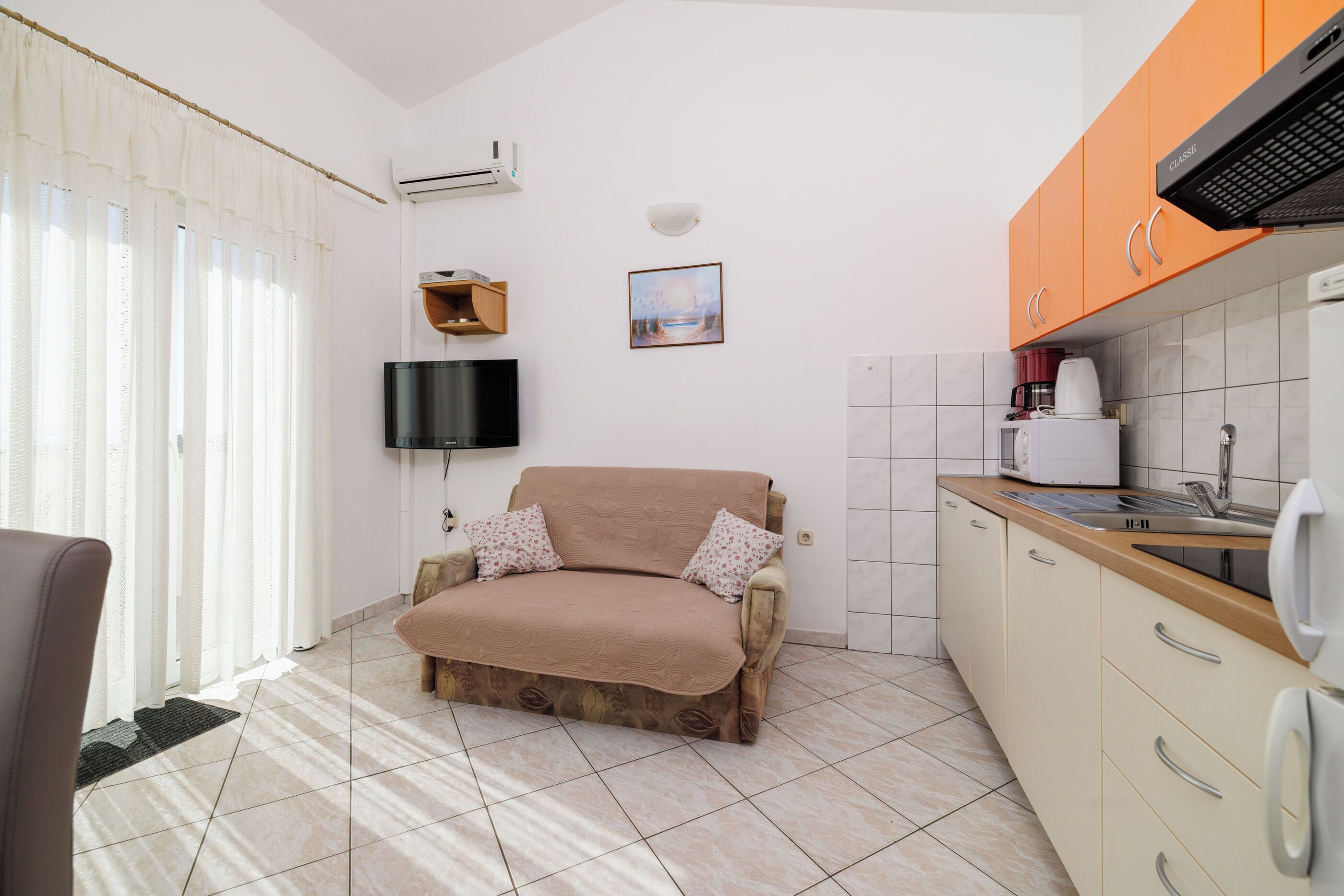 A compact living space with a sofa, a television, a kitchen area with cabinets and a sink, and a window with curtains.