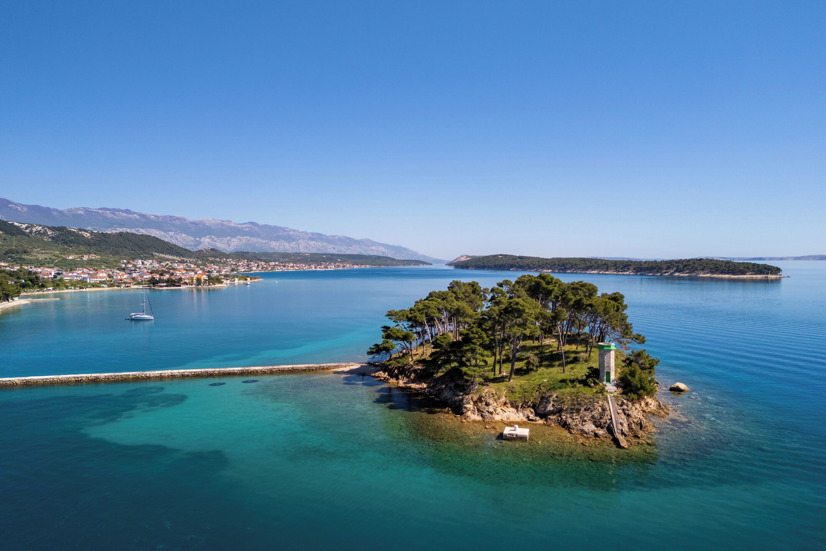 A coastal town with clear blue waters, a small island with trees, and a lighthouse.