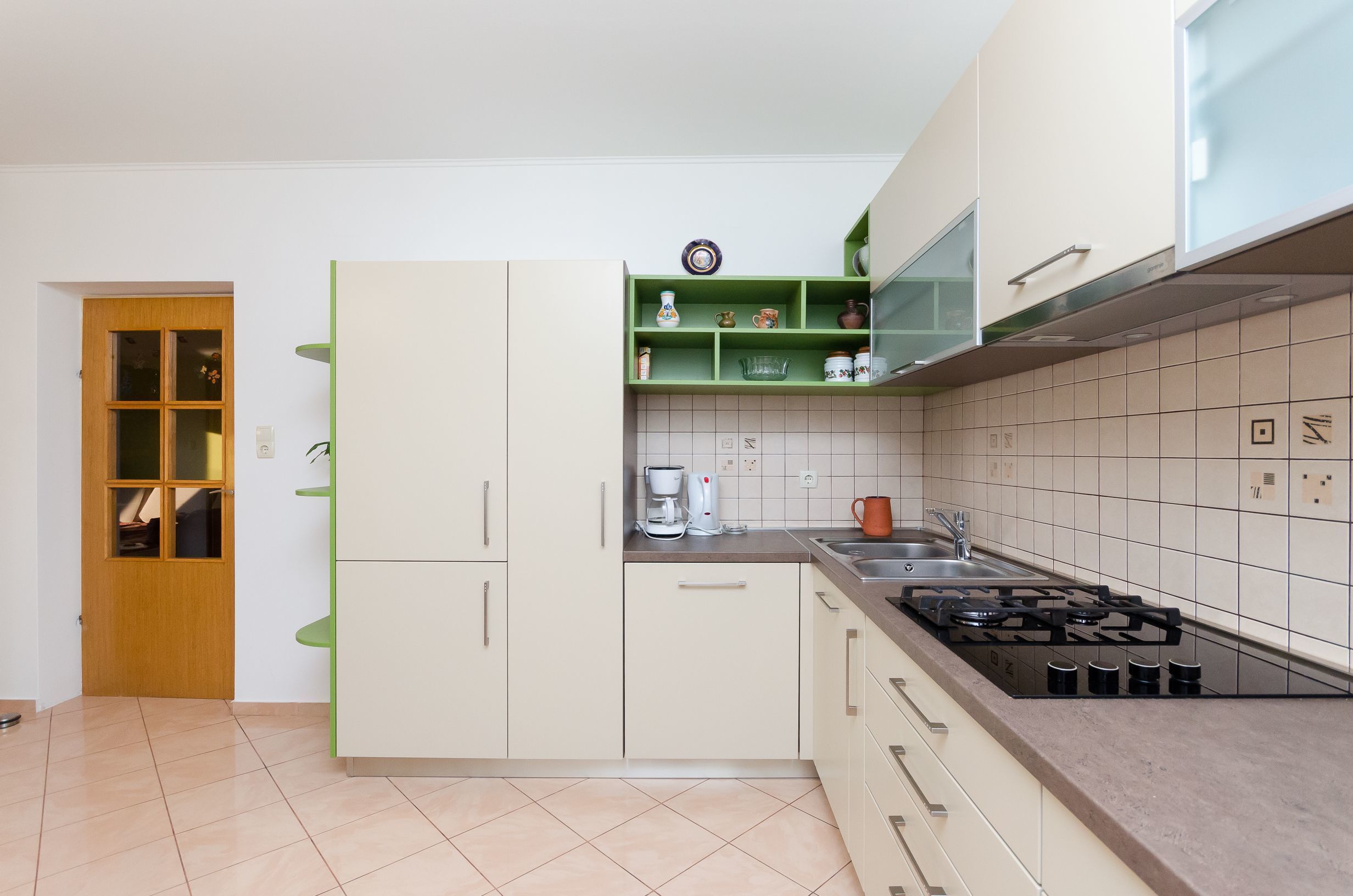 Une cuisine moderne avec des meubles blancs, une cuisinière à gaz et une étagère verte où sont rangés les ustensiles de cuisine.