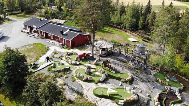 Un terrain de golf avec un bâtiment rouge, une structure en bois et un tracteur.