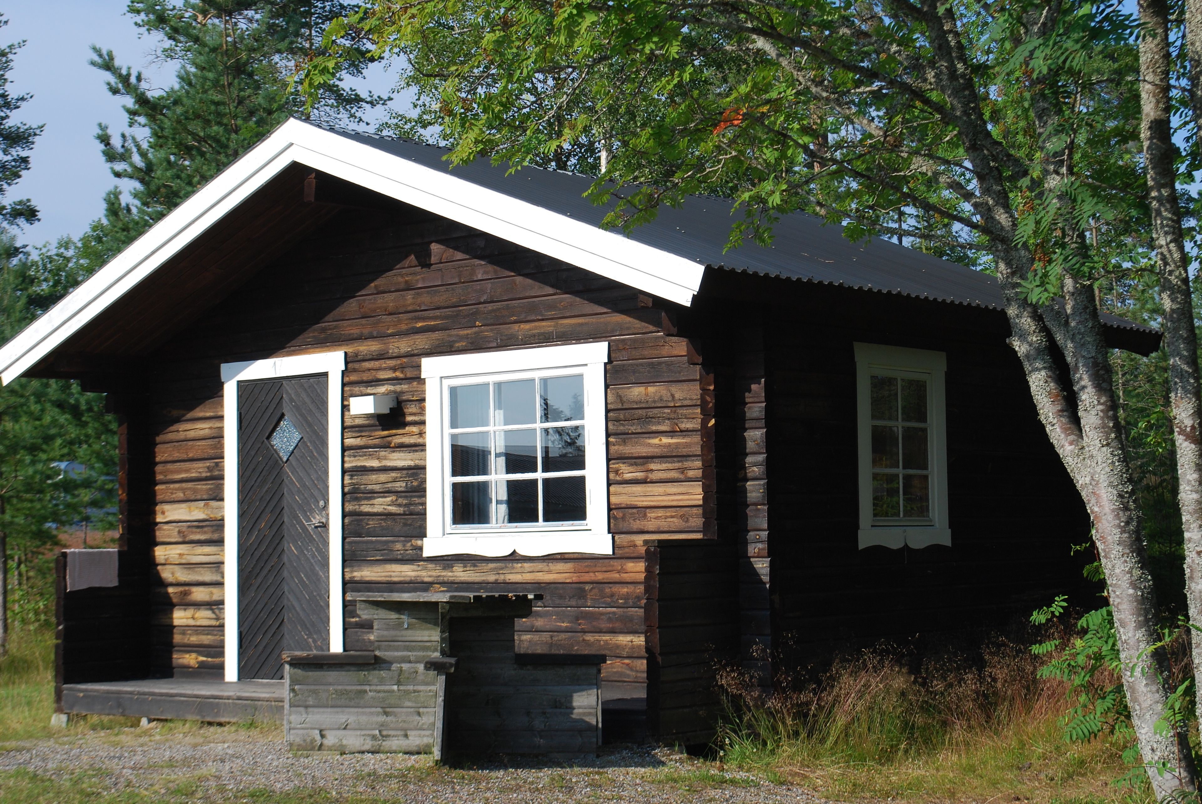 Une cabane en bois avec une porte d’entrée, une fenêtre et un petit porche.