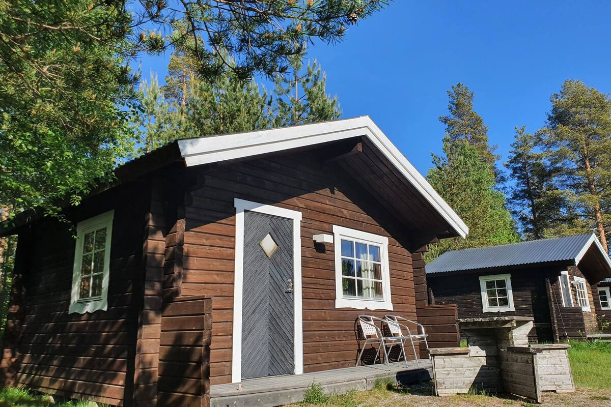 A small wooden cabin with a front porch, two windows, and a door.