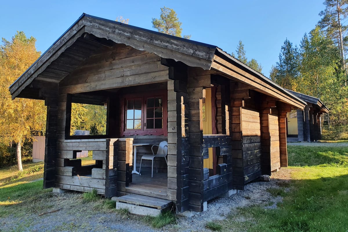 A rustic cabin with a porch, a small table, and a chair.
