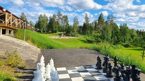 Un jeu d’échecs installé à l’extérieur, avec une forêt et un bâtiment en arrière-plan.