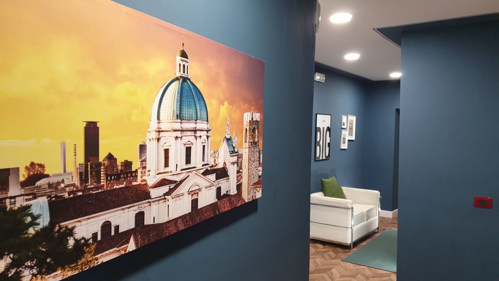 Um saguão de hotel com uma grande pintura de paisagem urbana, um sofá branco e uma parede azul.