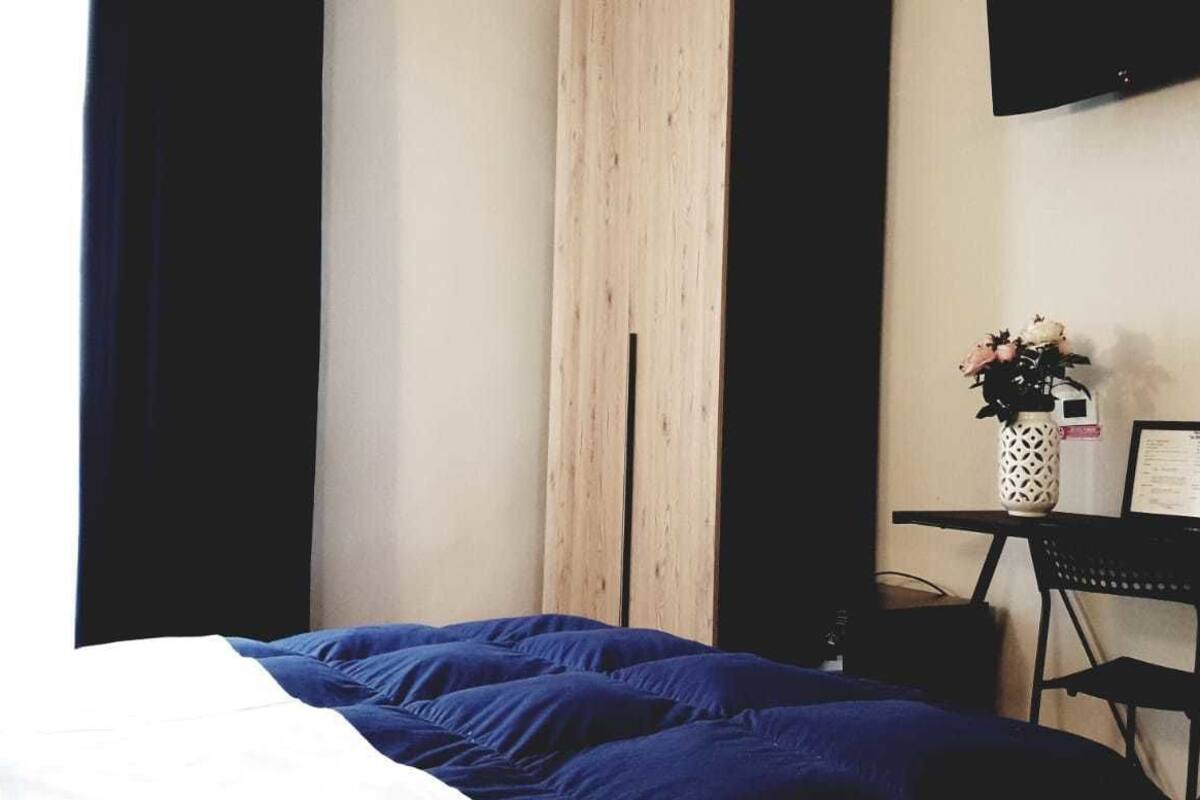 A bedroom with a bed, a desk with a chair, a vase with flowers, and a mounted TV.