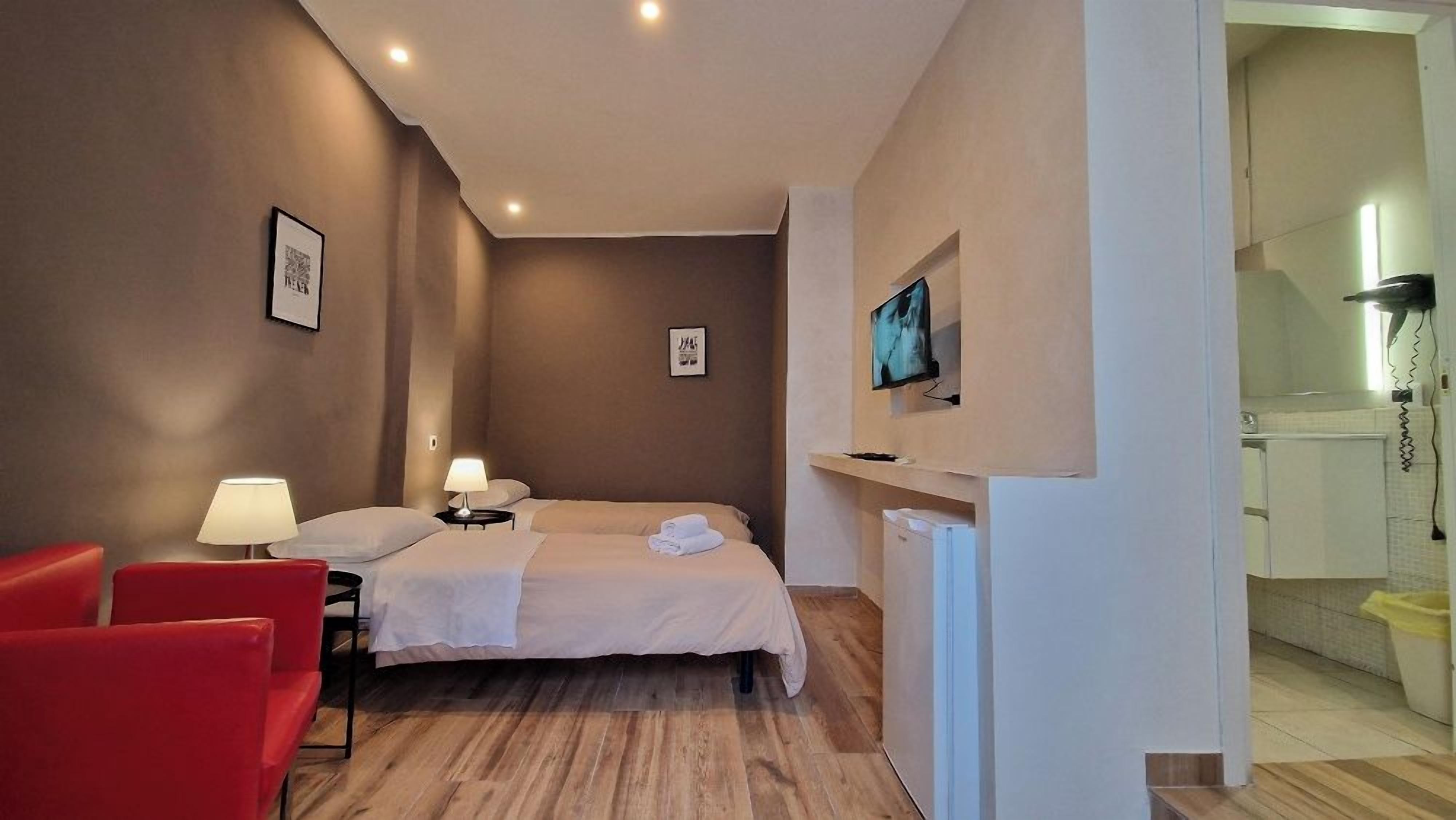 Ein Hotelzimmer mit einem Bett, zwei Nachttischlampen, einem roten Sessel, einem Fernseher und einem kleinen weißen Tisch.