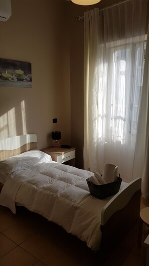 A bedroom with a bed, a nightstand, a lamp, and a window with sheer curtains. - Albergo La Svolta (Brescia)