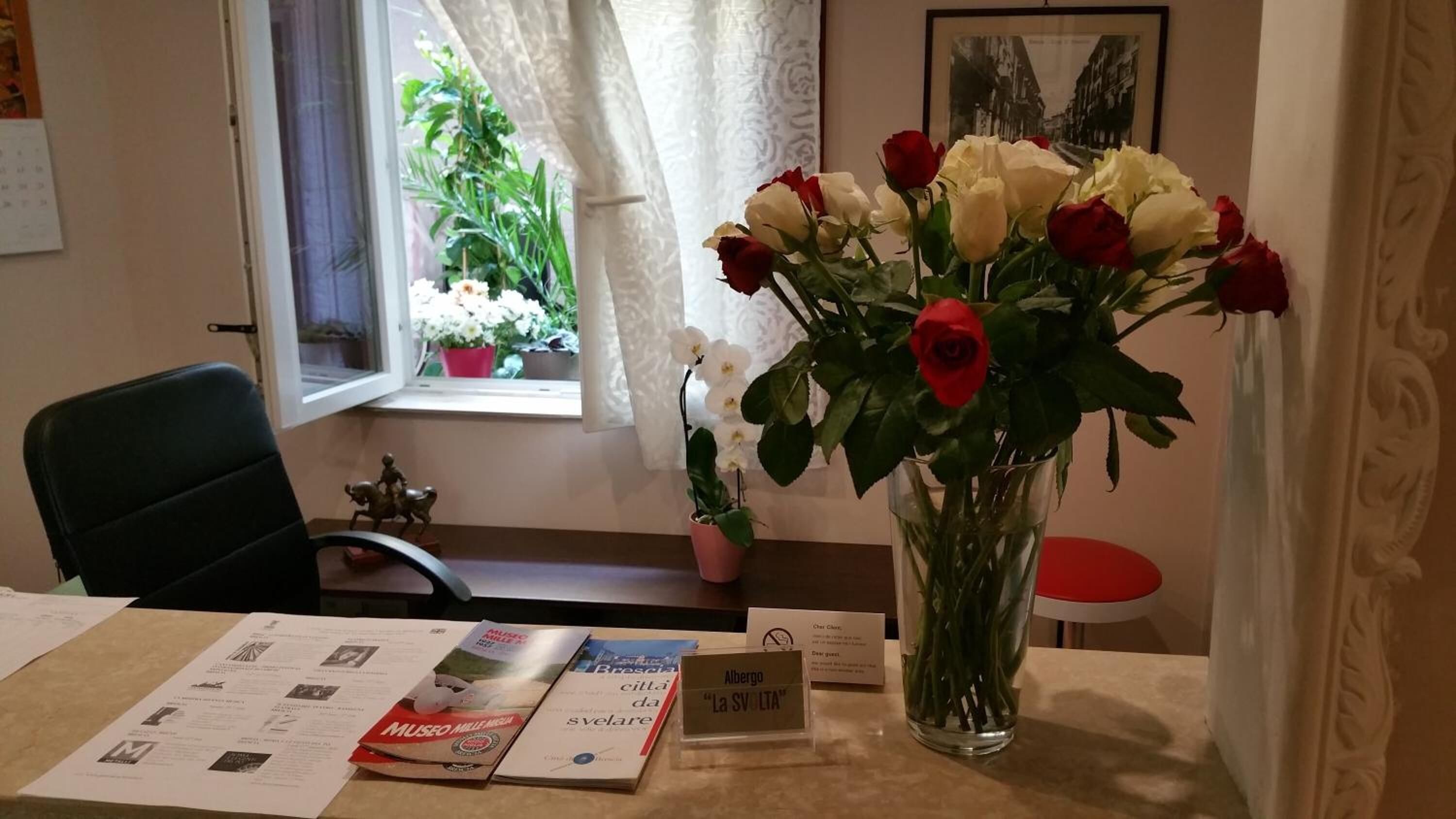 A reception desk with a vase of roses, a calendar, brochures, and a window with a view of a plant.