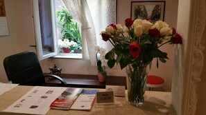 A reception desk with a vase of roses, a calendar, brochures, and a window with a view of a plant. - Albergo La Svolta (Brescia)