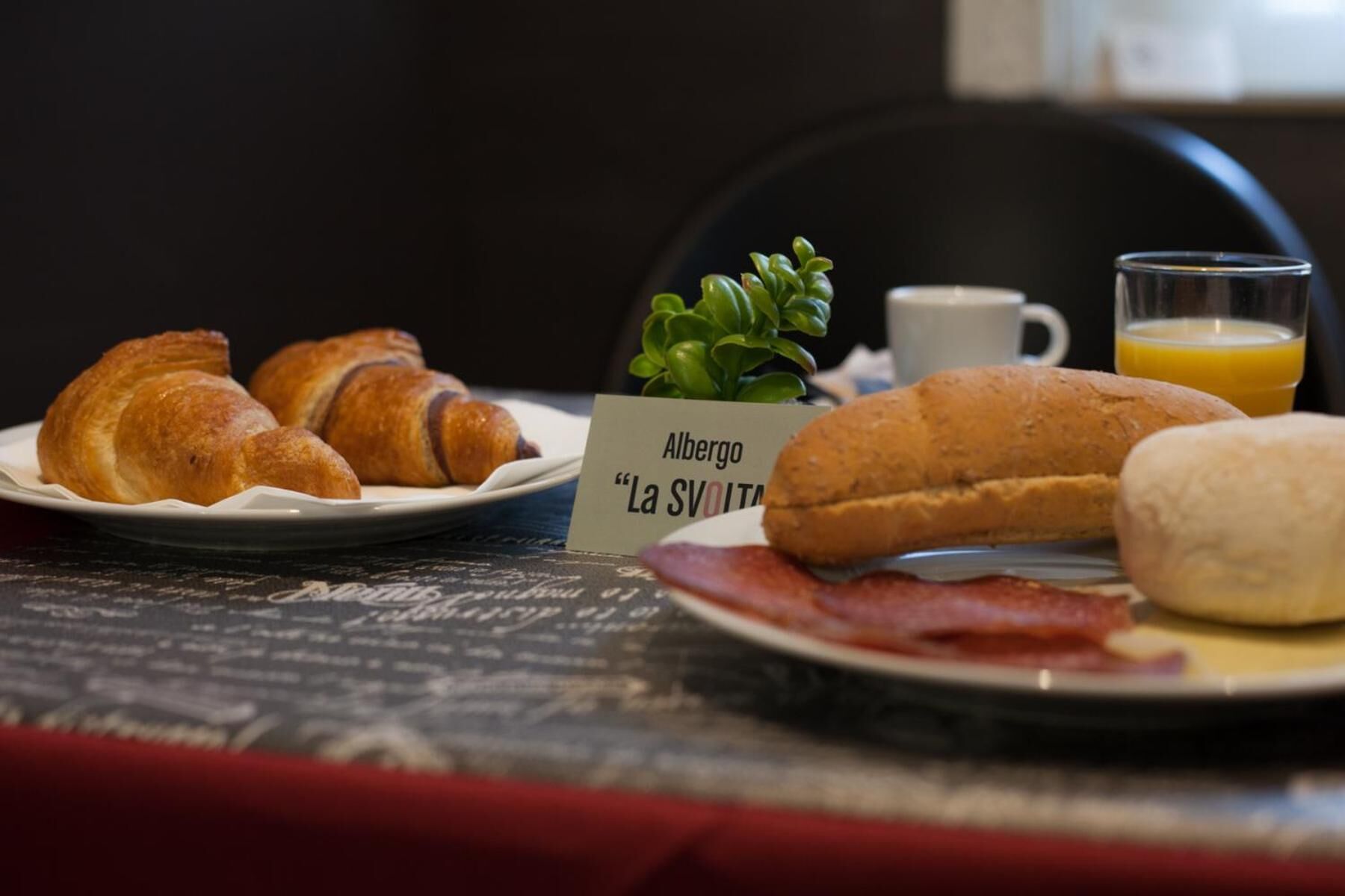 Una mesa de desayuno con cruasanes, un sándwich, tocino, una taza de café y un vaso de zumo de naranja.