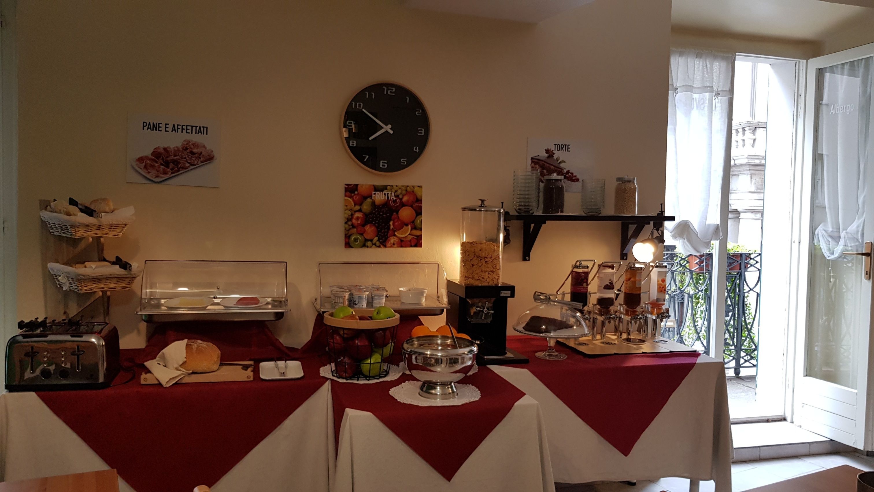 Montaje de un bufé de desayuno con un reloj, una presentación de frutas y diversas opciones de comida.