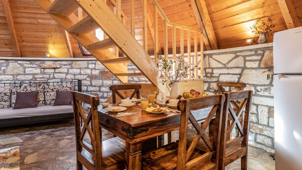 Una mesa de comedor de madera con sillas, una pared de piedra y una escalera.