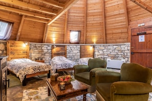 Interior acogedor de una cabaña de troncos con dos camas, una pared de piedra, vigas de madera en el techo y una chimenea de piedra.
