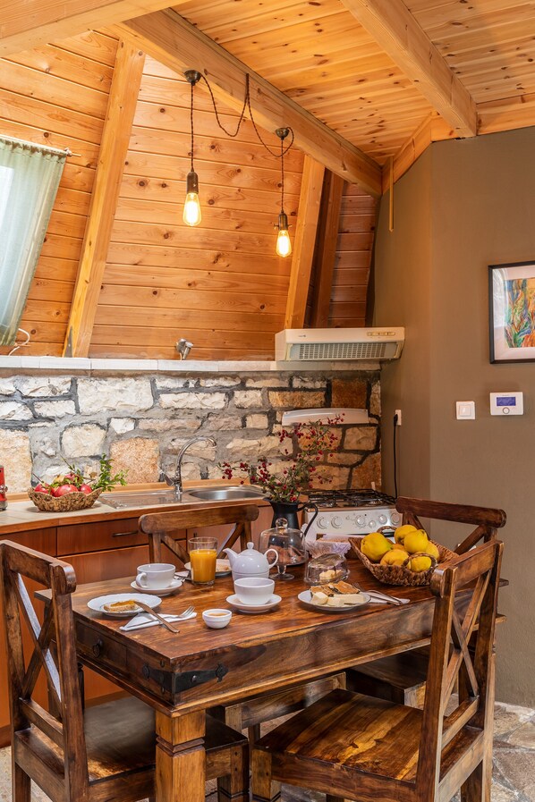 A wooden dining table with chairs, a stone wall, a kitchen area with a stove, and a hanging light fixture. - Theasis Igloo (Central Tzoumerka)