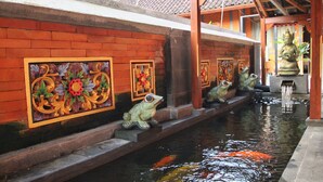 Ein traditionelles Gebäude mit einem Ziegeldach, einem Koiteich und verzierter Froschstatue am Ufer.