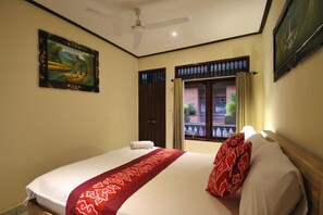 A hotel room with a bed, a ceiling fan, a window with curtains, and a painting on the wall. - Happy Inn (Ubud)