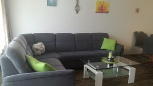 A modern living room with a grey sofa, green cushions, a glass coffee table, and a clock on the wall. - FeWo Paula (Oberstaufen)